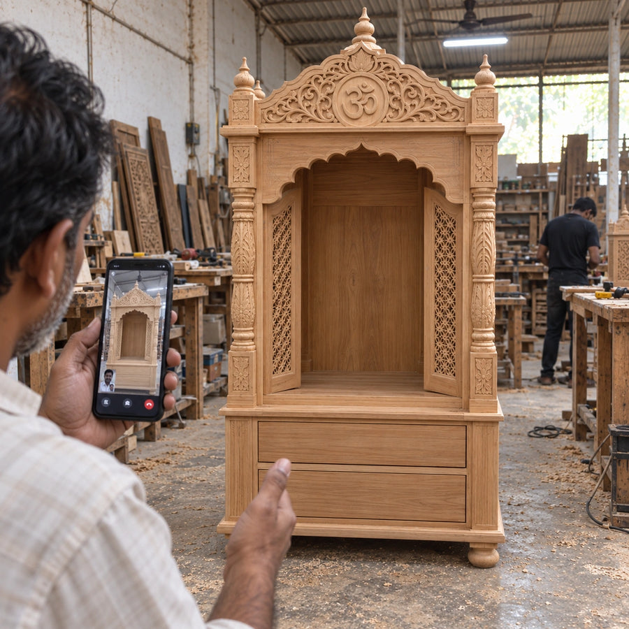 A hand-carved wooden pooja mandir in DZYN workshop setting, with a man holding a smartphone to take a photo in the foreground.