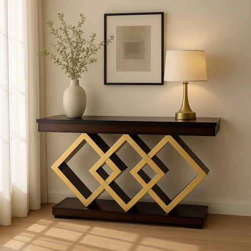 Modern console table with dark wooden top and geometric gold diamond-shaped base, styled against a beige wall with a vase, lamp, and framed artwork under soft natural light.