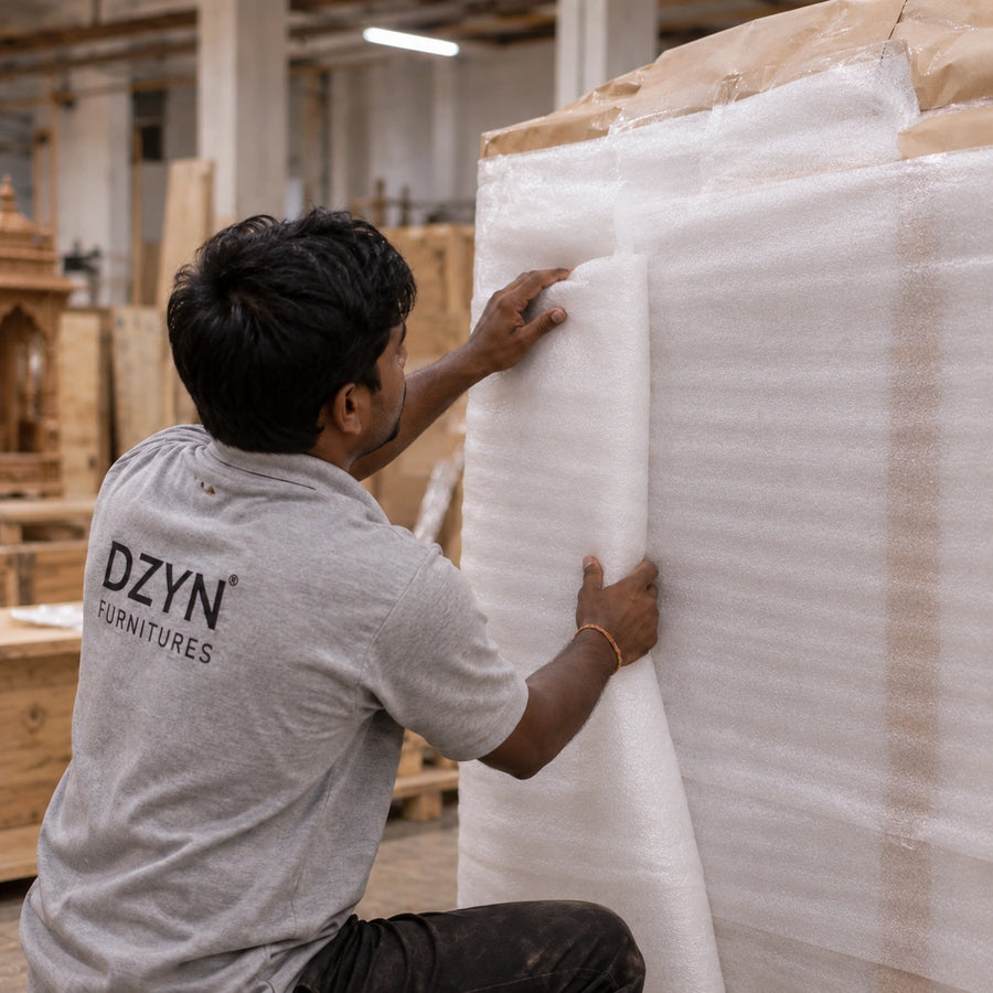 A man wearing a gray DZYN Furnitures t-shirt is wrapping the mandir.